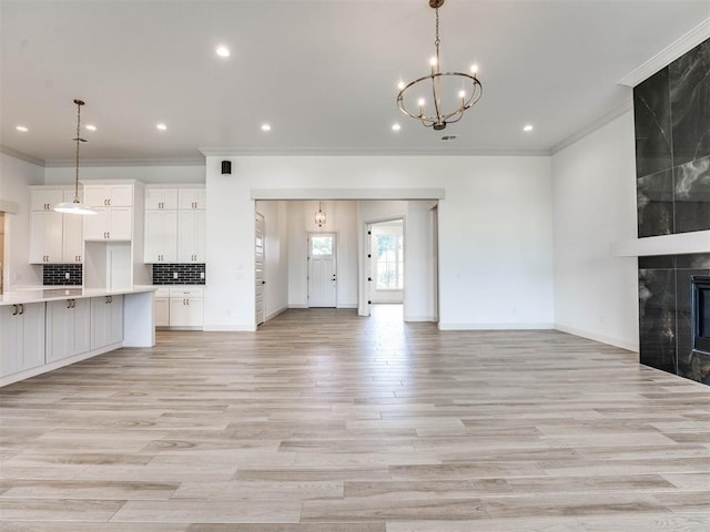 unfurnished living room featuring a chandelier, a fireplace, ornamental molding, and light hardwood / wood-style flooring