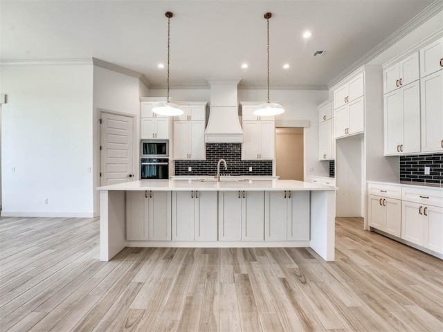 kitchen with backsplash, a kitchen island with sink, sink, hanging light fixtures, and custom range hood