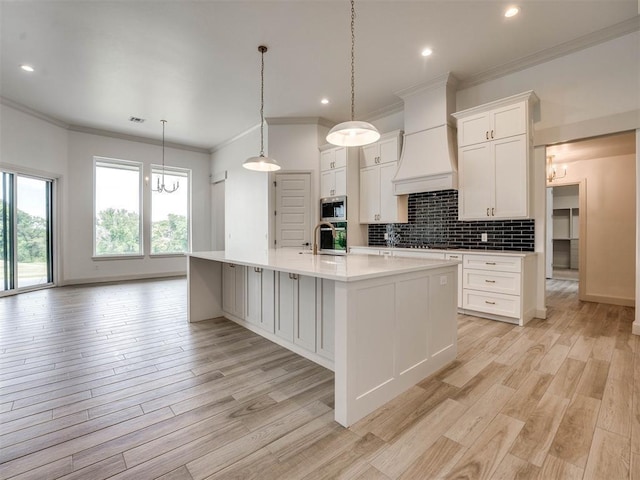 kitchen with white cabinetry, a kitchen island with sink, custom range hood, and appliances with stainless steel finishes