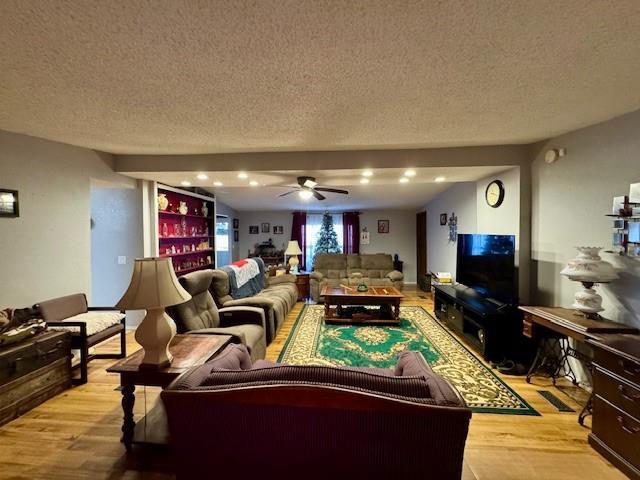 living room featuring a textured ceiling, light wood-type flooring, and ceiling fan