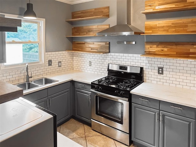 kitchen featuring sink, hanging light fixtures, wall chimney range hood, stainless steel gas range oven, and gray cabinets