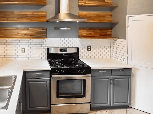 kitchen featuring gray cabinetry, wall chimney range hood, gas range, tasteful backsplash, and light stone counters