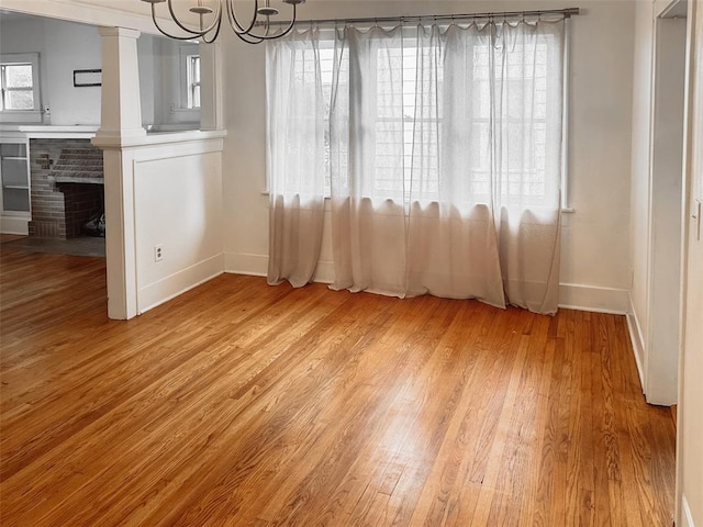 unfurnished dining area featuring light hardwood / wood-style floors, a fireplace, and an inviting chandelier