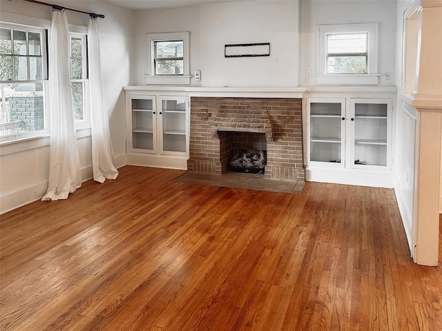 unfurnished living room featuring wood-type flooring and a brick fireplace