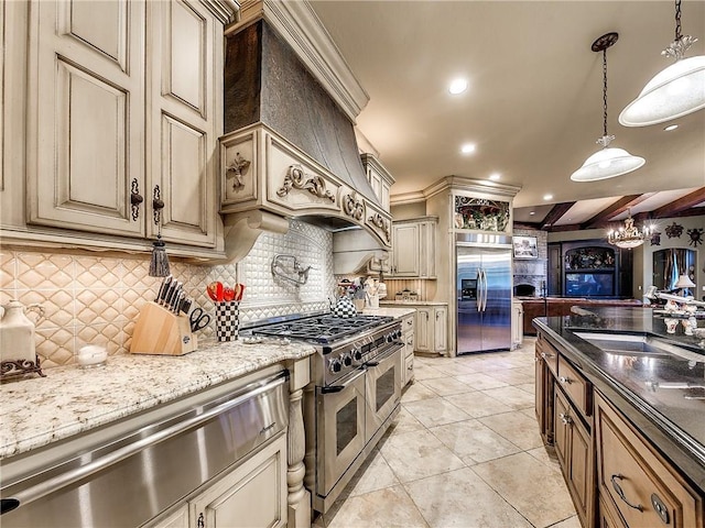 kitchen with appliances with stainless steel finishes, premium range hood, dark stone counters, pendant lighting, and cream cabinets