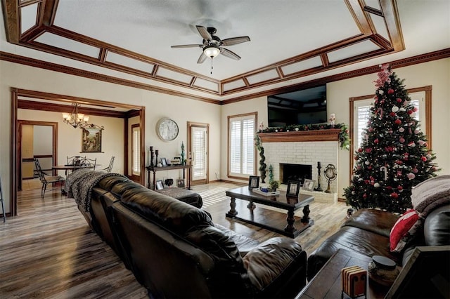 living room with crown molding, wood-type flooring, ceiling fan with notable chandelier, and a brick fireplace