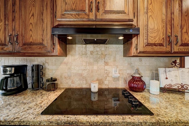 kitchen with decorative backsplash, light stone counters, black electric cooktop, and custom range hood