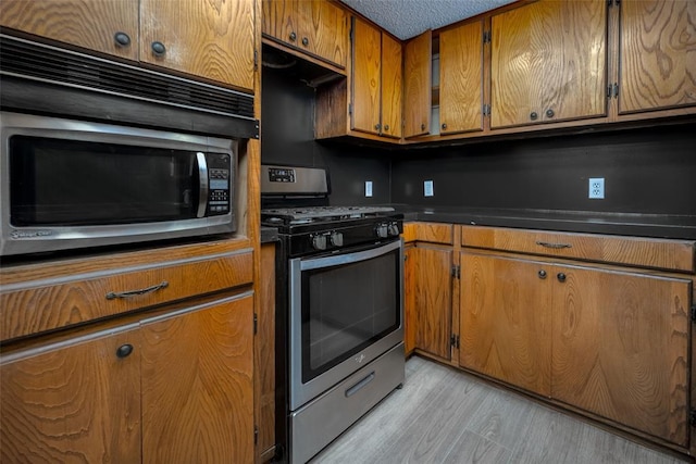 kitchen featuring ventilation hood, light hardwood / wood-style flooring, a textured ceiling, and appliances with stainless steel finishes