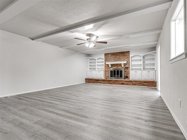 unfurnished living room with a fireplace, a textured ceiling, ceiling fan, beamed ceiling, and light hardwood / wood-style floors