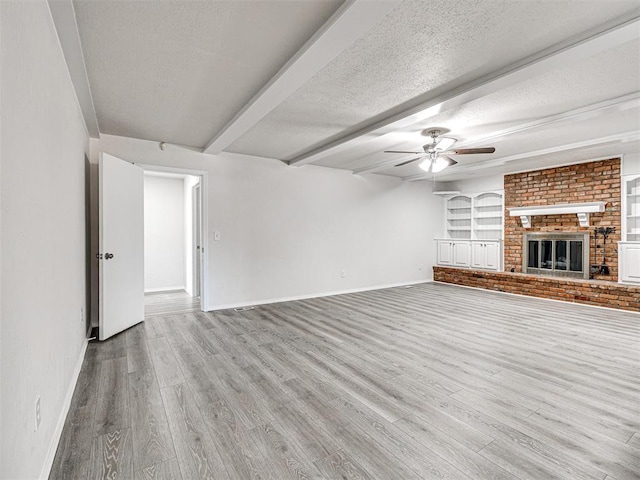 unfurnished living room with light hardwood / wood-style flooring, ceiling fan, built in features, a fireplace, and a textured ceiling