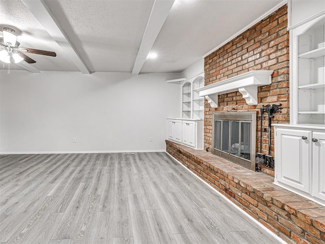 unfurnished living room featuring beam ceiling, ceiling fan, a brick fireplace, a textured ceiling, and light wood-type flooring