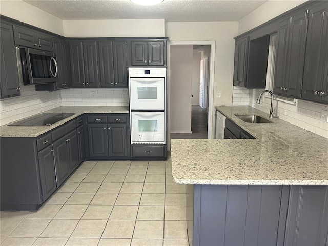 kitchen with kitchen peninsula, light stone counters, white double oven, black electric cooktop, and sink