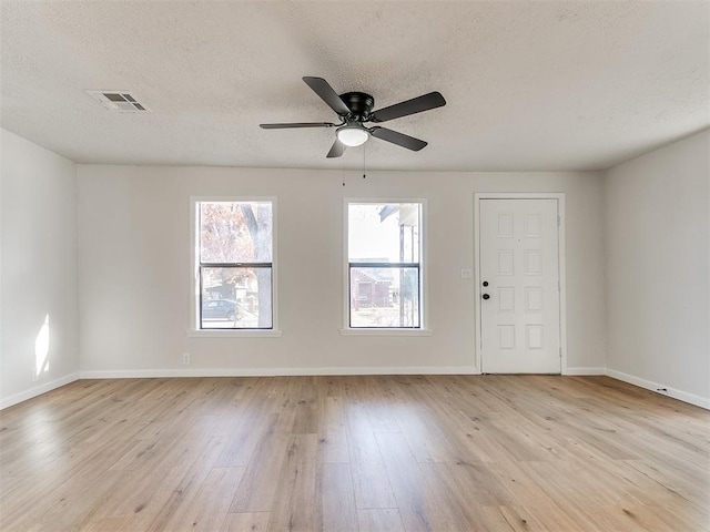 empty room featuring a textured ceiling, light wood-type flooring, and ceiling fan