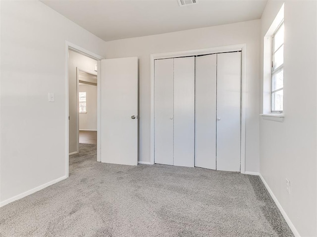 unfurnished bedroom featuring multiple windows, light carpet, and a closet