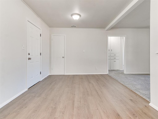 spare room featuring beamed ceiling and light colored carpet