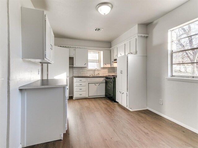 kitchen with tasteful backsplash, black gas range oven, sink, light hardwood / wood-style floors, and white cabinetry