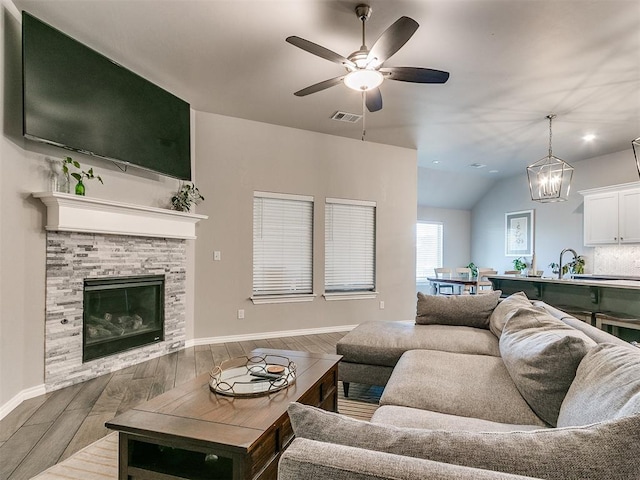 living room with lofted ceiling, ceiling fan with notable chandelier, sink, hardwood / wood-style flooring, and a fireplace