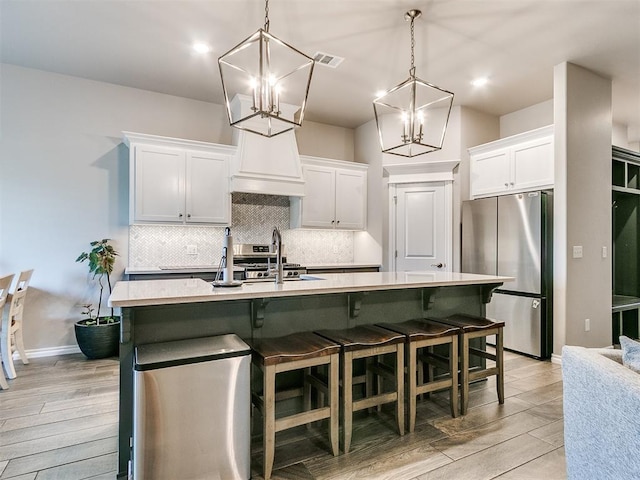 kitchen featuring pendant lighting, white cabinets, a center island with sink, light hardwood / wood-style floors, and stainless steel appliances