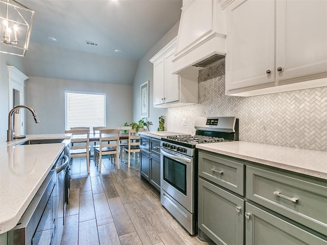 kitchen featuring white cabinetry, hanging light fixtures, tasteful backsplash, appliances with stainless steel finishes, and light wood-type flooring