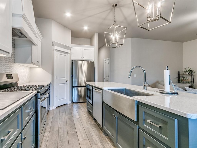 kitchen featuring a kitchen island with sink, white cabinets, sink, stainless steel appliances, and a chandelier