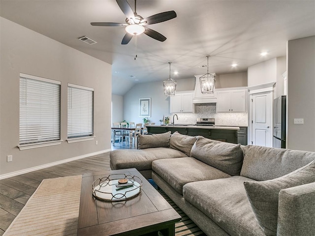 living room featuring hardwood / wood-style floors, ceiling fan with notable chandelier, lofted ceiling, and sink