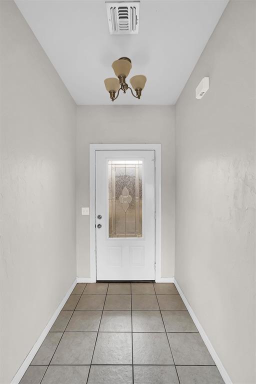 doorway to outside with light tile patterned floors and a chandelier