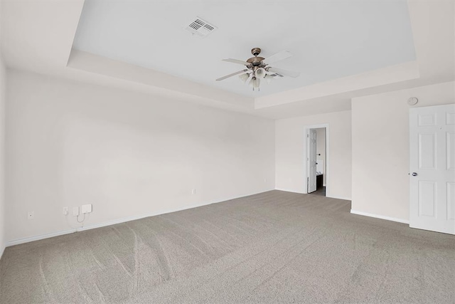 empty room featuring a raised ceiling, ceiling fan, and carpet floors