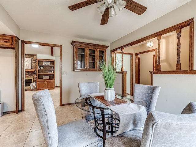 dining room with built in shelves, ceiling fan, a fireplace, and light tile patterned flooring