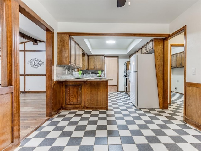 kitchen with kitchen peninsula, a tray ceiling, ceiling fan, dark wood-type flooring, and white refrigerator