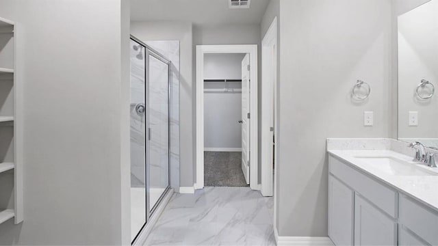 full bath with visible vents, vanity, baseboards, a stall shower, and a walk in closet