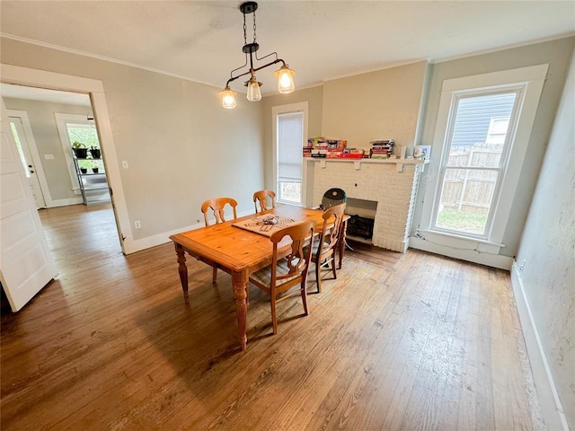 dining area featuring a brick fireplace, hardwood / wood-style floors, ornamental molding, and a notable chandelier