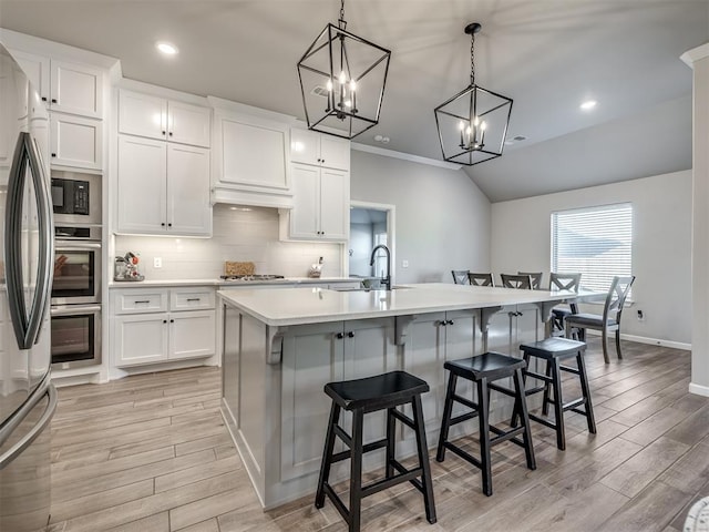 kitchen featuring vaulted ceiling, a breakfast bar, pendant lighting, white cabinets, and a kitchen island with sink