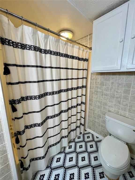 bathroom featuring toilet, a textured ceiling, tile patterned floors, and curtained shower