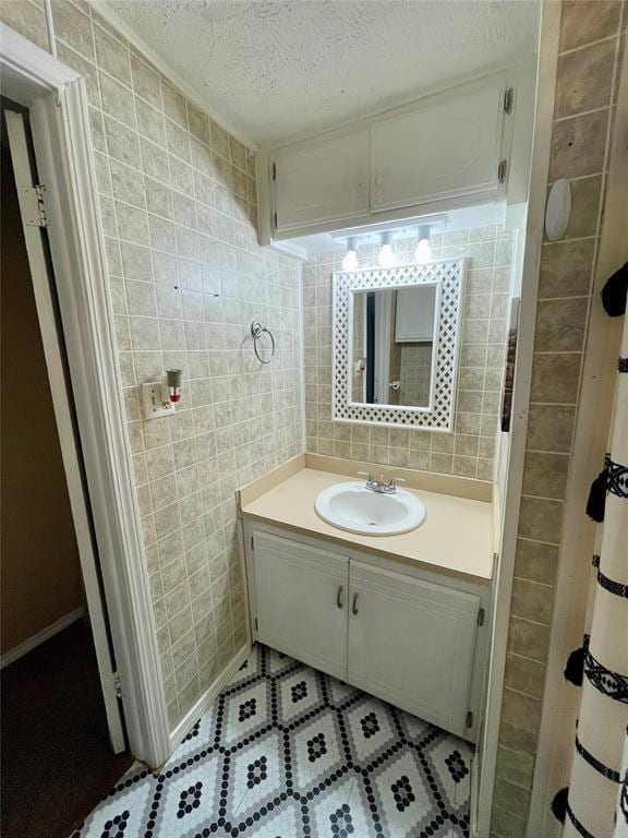 bathroom featuring a textured ceiling, vanity, and tile walls