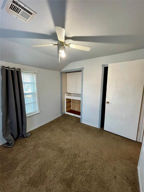 unfurnished bedroom featuring dark colored carpet, a textured ceiling, vaulted ceiling, and ceiling fan