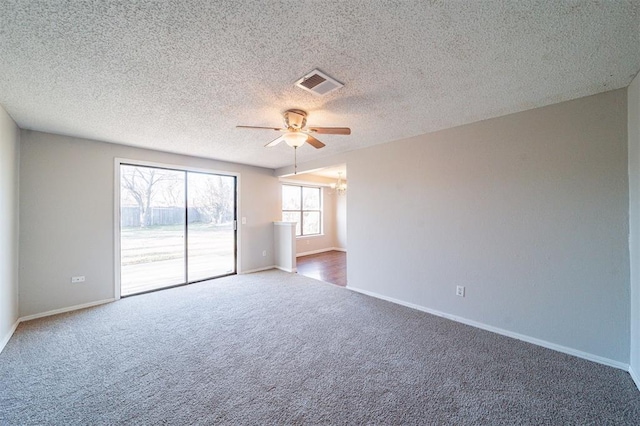 empty room featuring ceiling fan with notable chandelier, a textured ceiling, and dark carpet