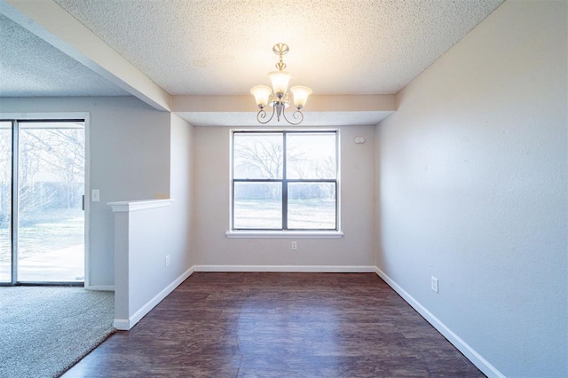 empty room with a notable chandelier, a wealth of natural light, dark hardwood / wood-style floors, and a textured ceiling