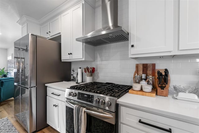 kitchen featuring decorative backsplash, appliances with stainless steel finishes, wall chimney exhaust hood, light hardwood / wood-style floors, and white cabinetry