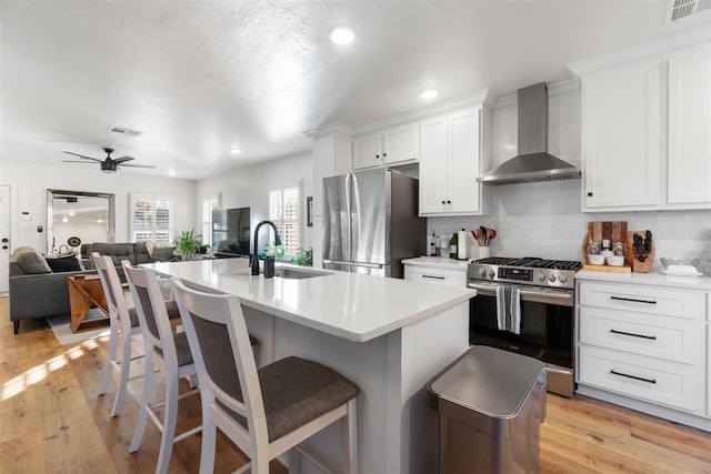 kitchen with white cabinets, wall chimney range hood, appliances with stainless steel finishes, and light hardwood / wood-style flooring