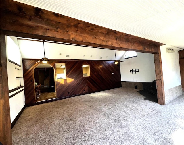 unfurnished living room with lofted ceiling with beams, ceiling fan, carpet flooring, and wooden walls