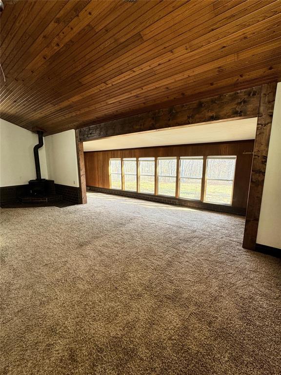 additional living space featuring carpet floors, a wealth of natural light, wooden ceiling, and a wood stove