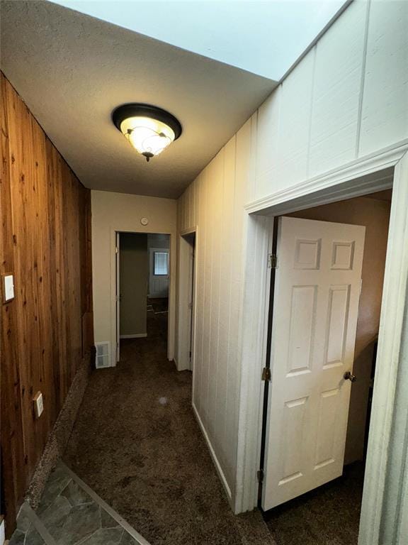 hallway featuring visible vents, wooden walls, and dark carpet