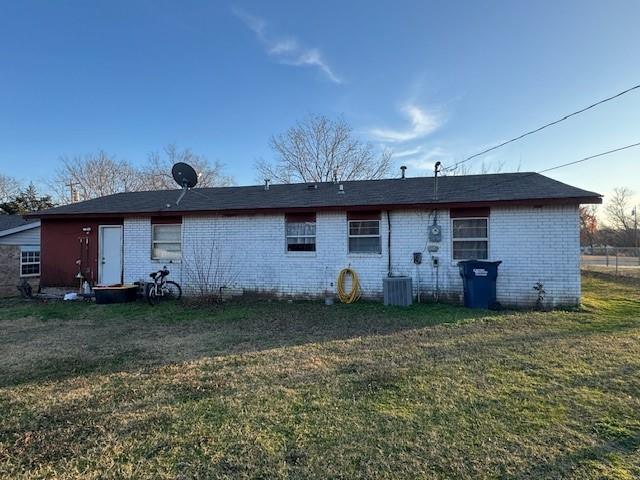 rear view of house featuring brick siding, cooling unit, and a yard