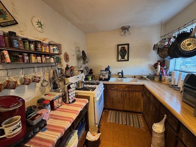 kitchen featuring brown cabinets, white range with gas stovetop, light countertops, and a sink