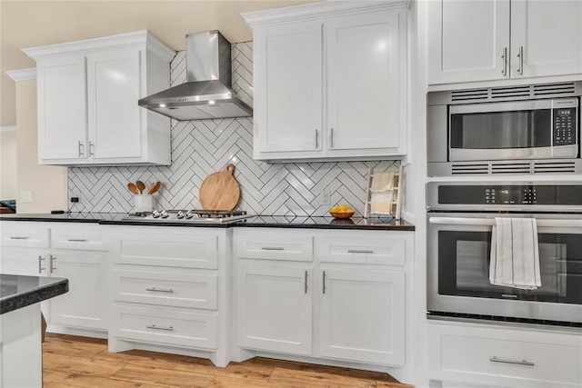 kitchen featuring decorative backsplash, wall chimney exhaust hood, stainless steel appliances, light hardwood / wood-style flooring, and white cabinetry