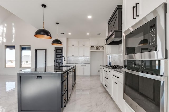 kitchen with tasteful backsplash, a kitchen island with sink, sink, white cabinets, and hanging light fixtures