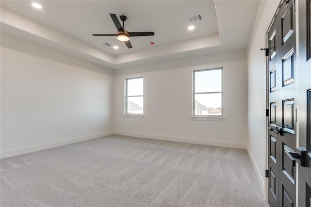 empty room featuring a raised ceiling, ceiling fan, and light colored carpet