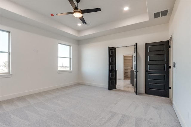 empty room with light carpet, a tray ceiling, and ceiling fan