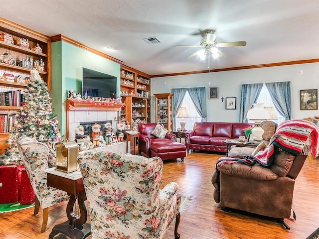 living room featuring built in shelves, ceiling fan, wood-type flooring, and crown molding