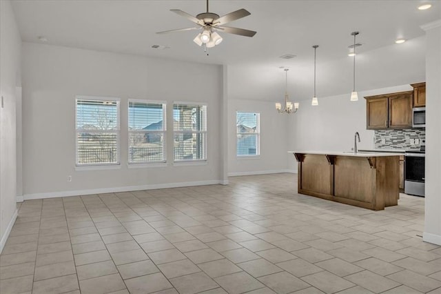 kitchen with appliances with stainless steel finishes, decorative backsplash, a center island with sink, ceiling fan with notable chandelier, and decorative light fixtures